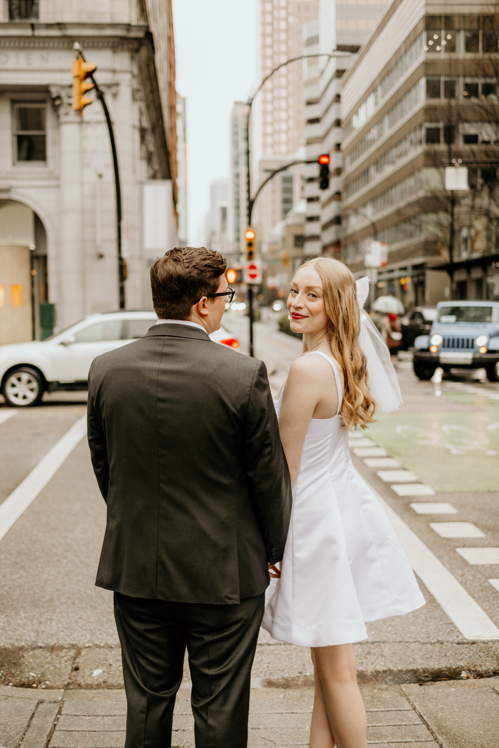 A couple crosses a busy Vancouver street, hand in hand during their downtown engagement session.